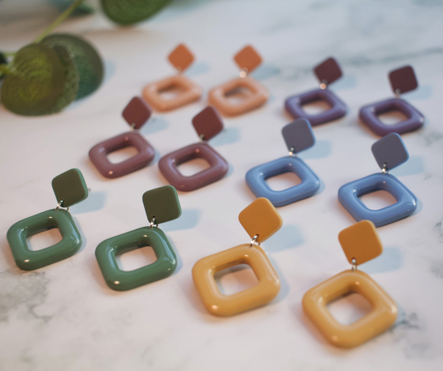 A collection of colorful square-shaped earrings on a marble surface