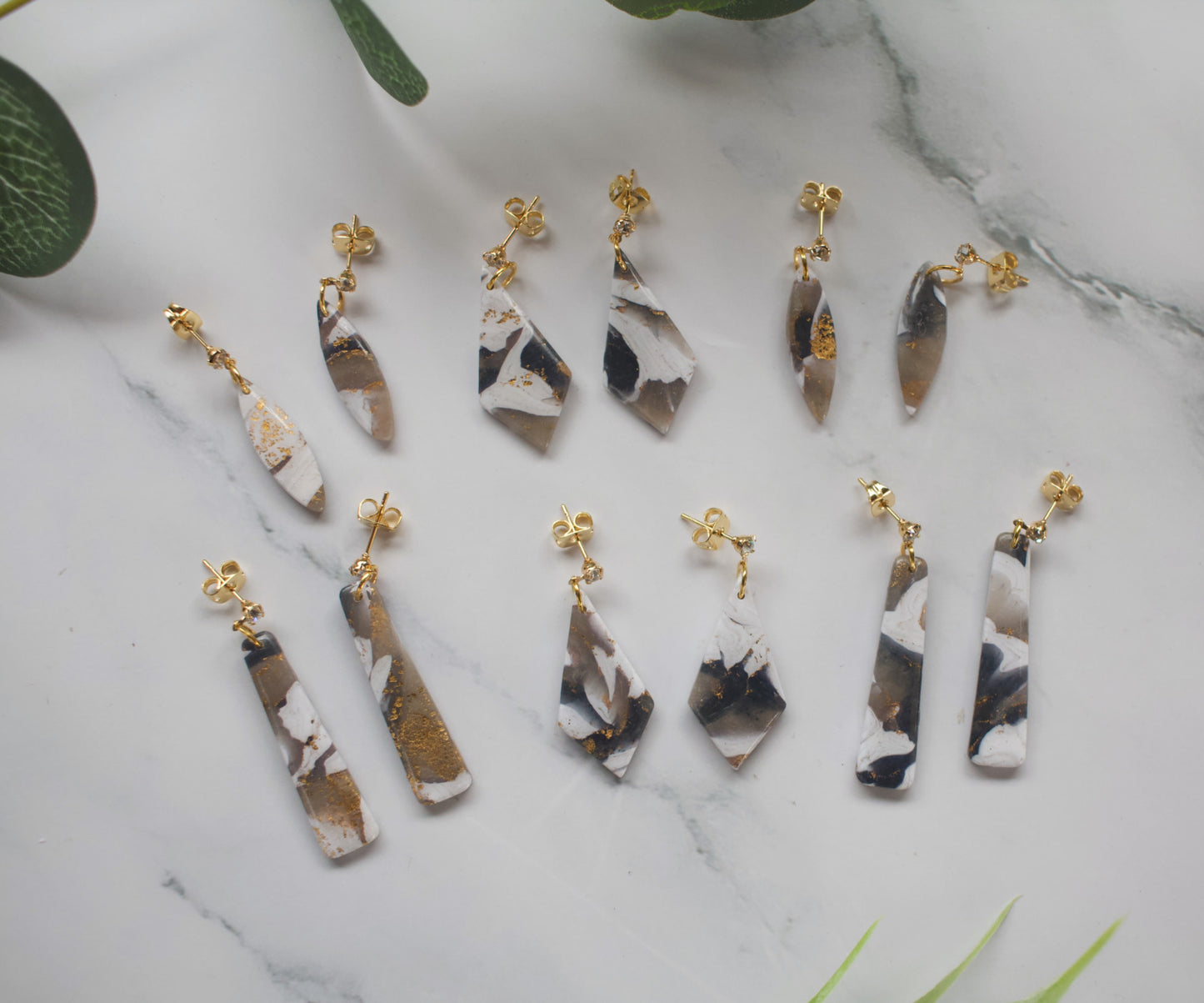 Collection of black and white marble-patterned earrings with gold accents on a marble surface