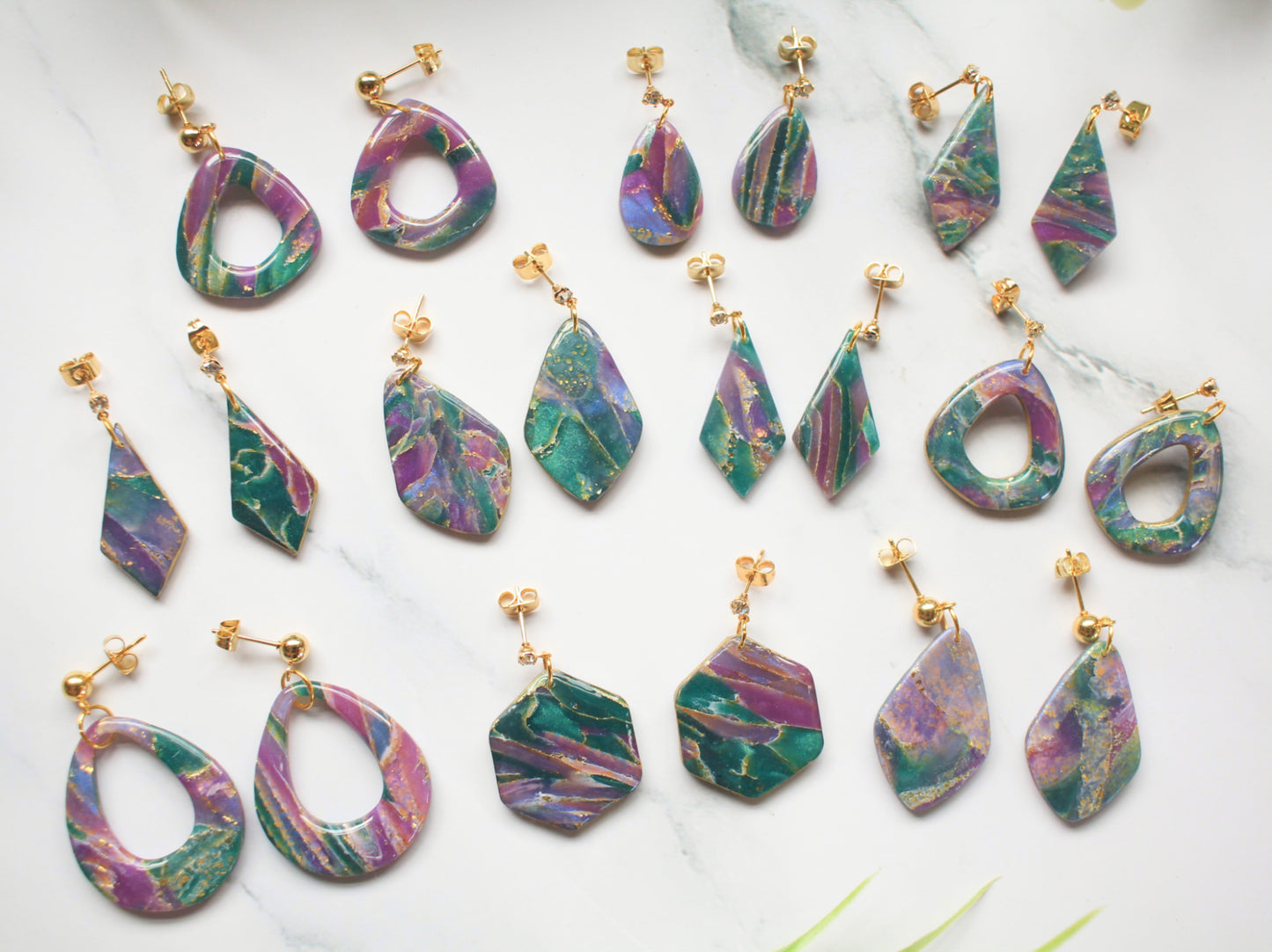 Purple, teal and gold marbled earring collection on a white background