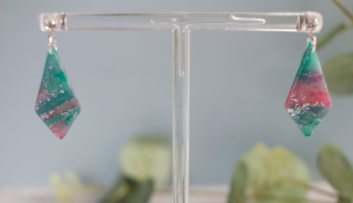Multicolored teardrop earrings on a clear stand with a blurred green plant background
