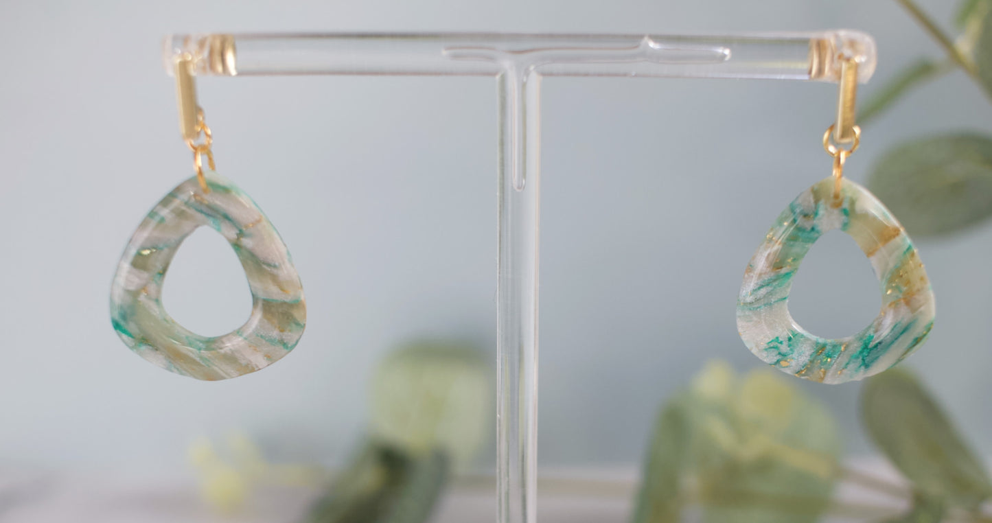 Pair of marbled green and gold earrings on a clear stand with a blurred background