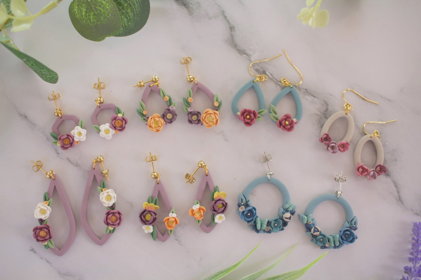 Collection of colorful floral earrings on a marble surface with green leaves.