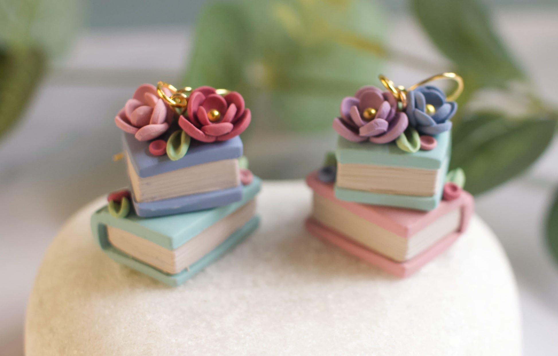 Colorful flower-shaped earrings on a white stand with green leaves in the background