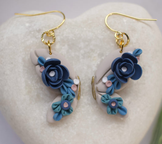 Pair of blue floral butterfly wing earrings on a heart-shaped stone background