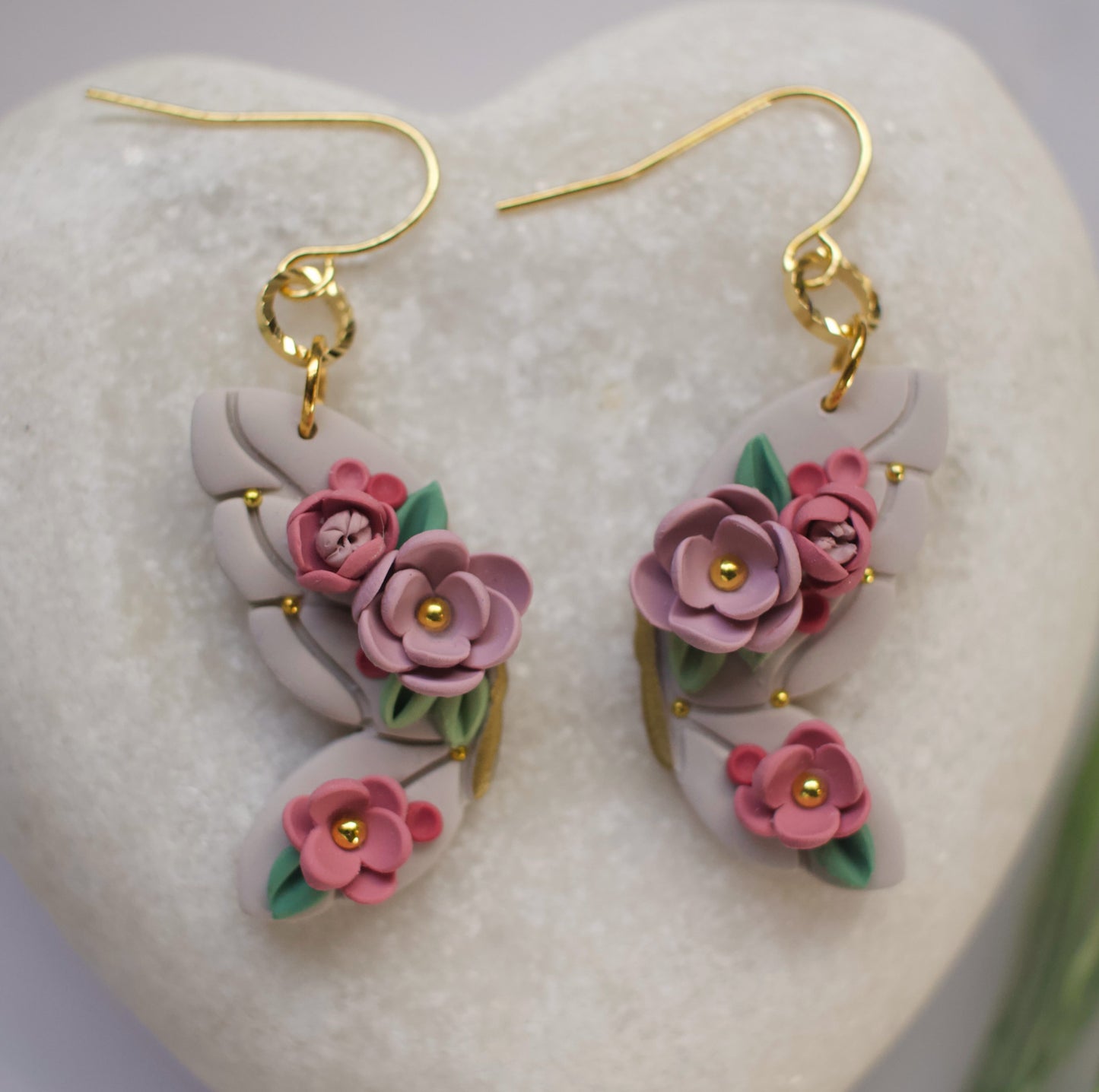 Floral butterfly earrings with pink flowers and gold accents on a heart-shaped stone.