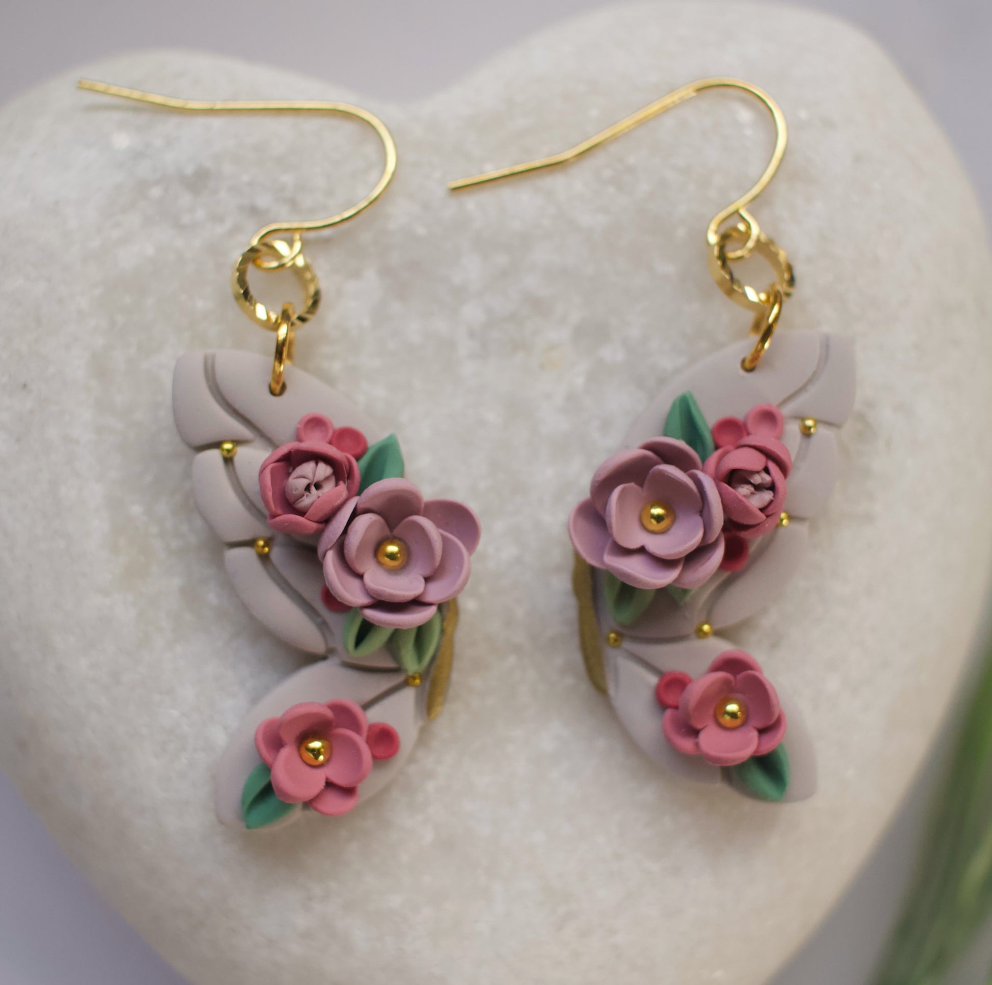 Floral butterfly earrings with pink flowers and gold accents on a heart-shaped stone.