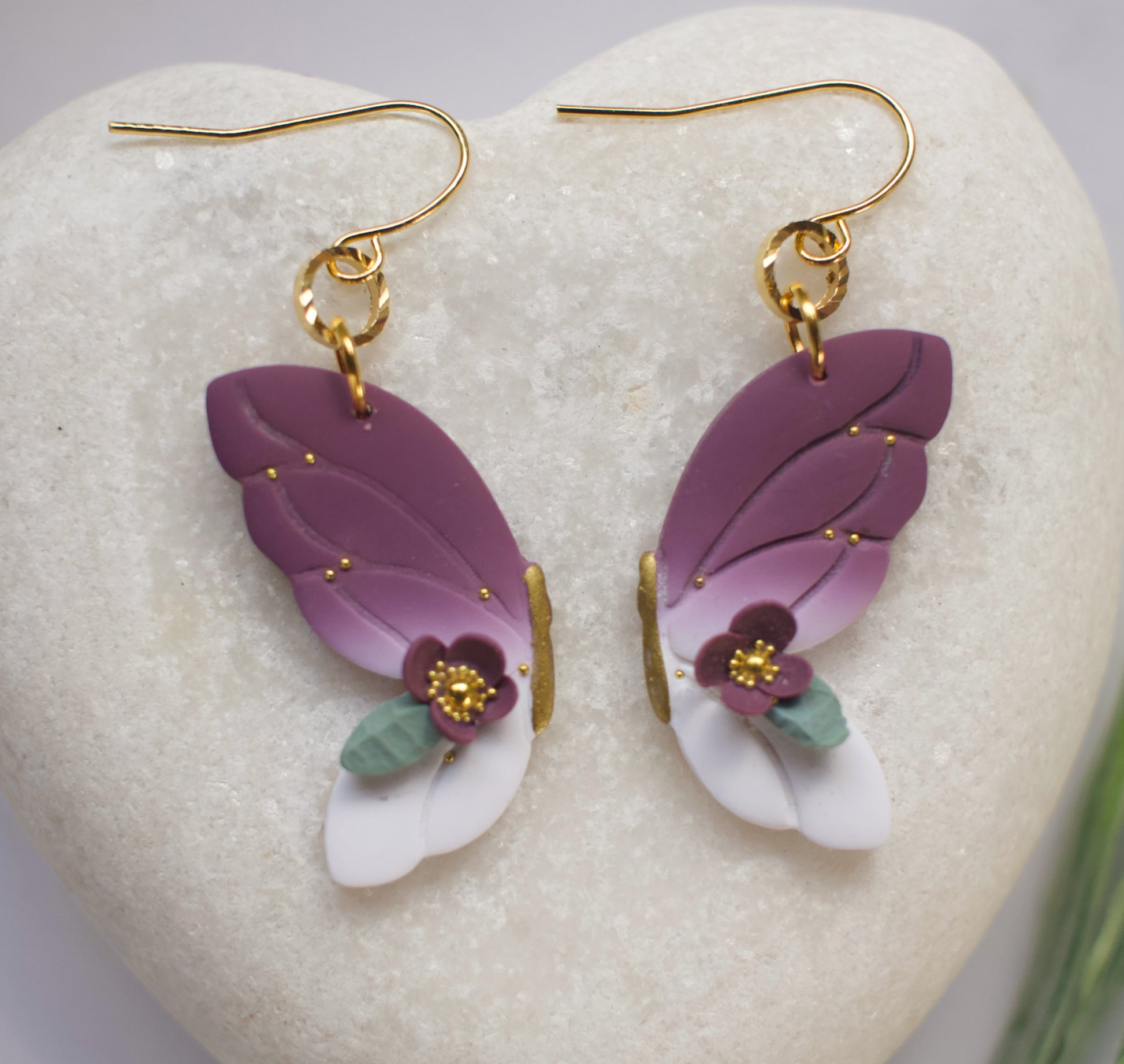 Purple and white butterfly earrings with floral details on a heart-shaped stone.