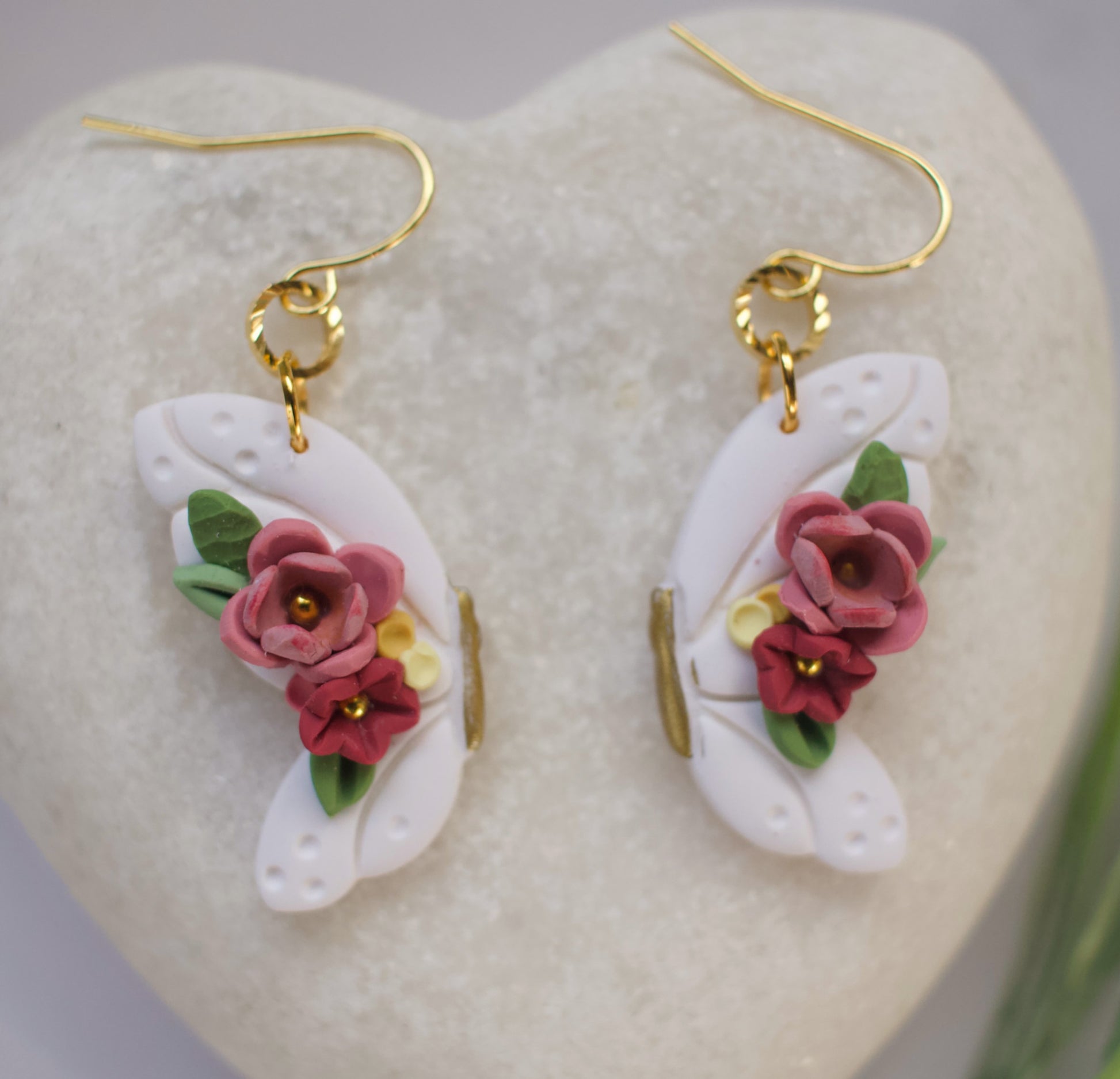 Floral butterfly earrings with pink flowers and gold accents on a heart-shaped stone background