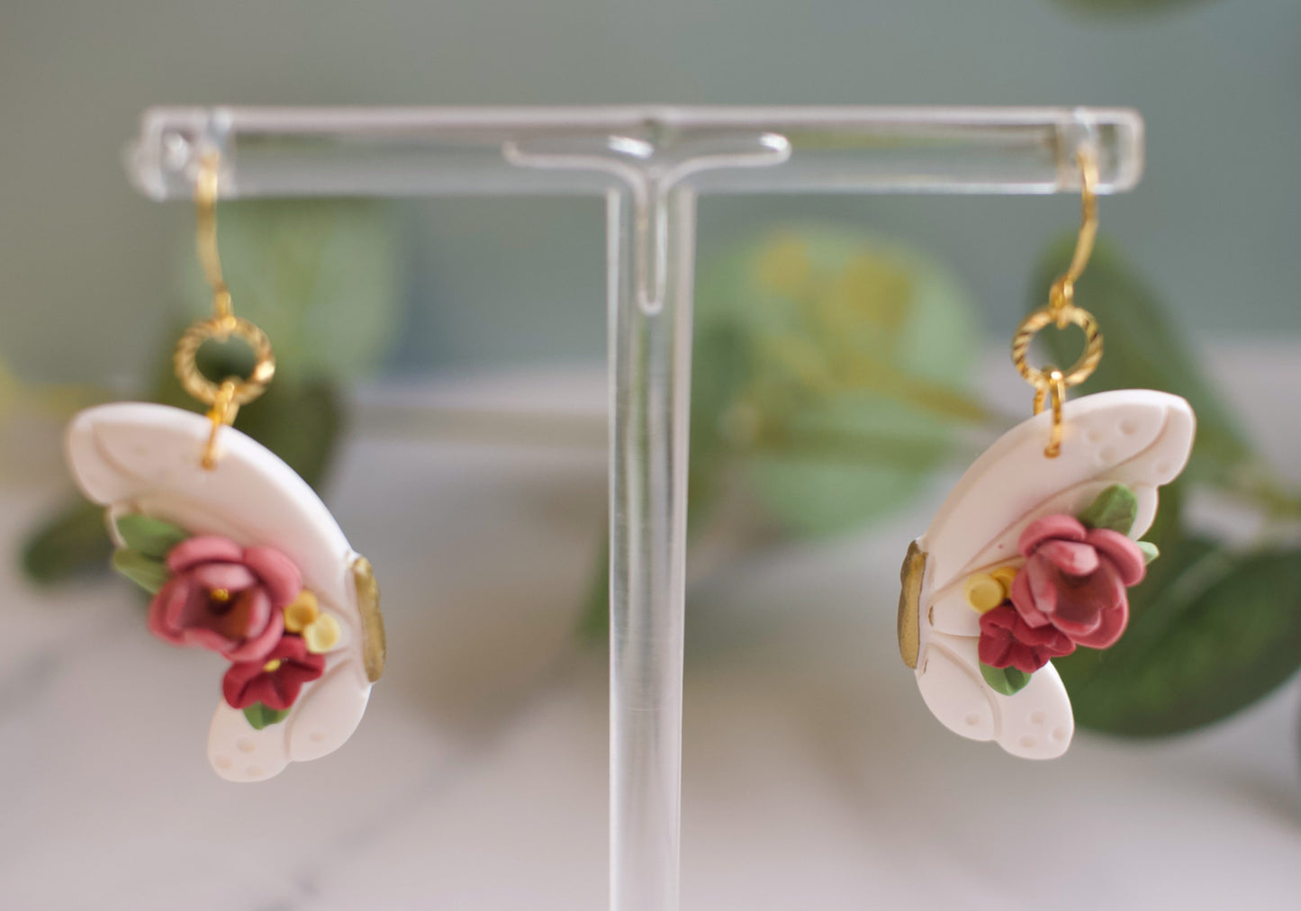 Floral butterfly earrings on a clear stand with a blurred green background