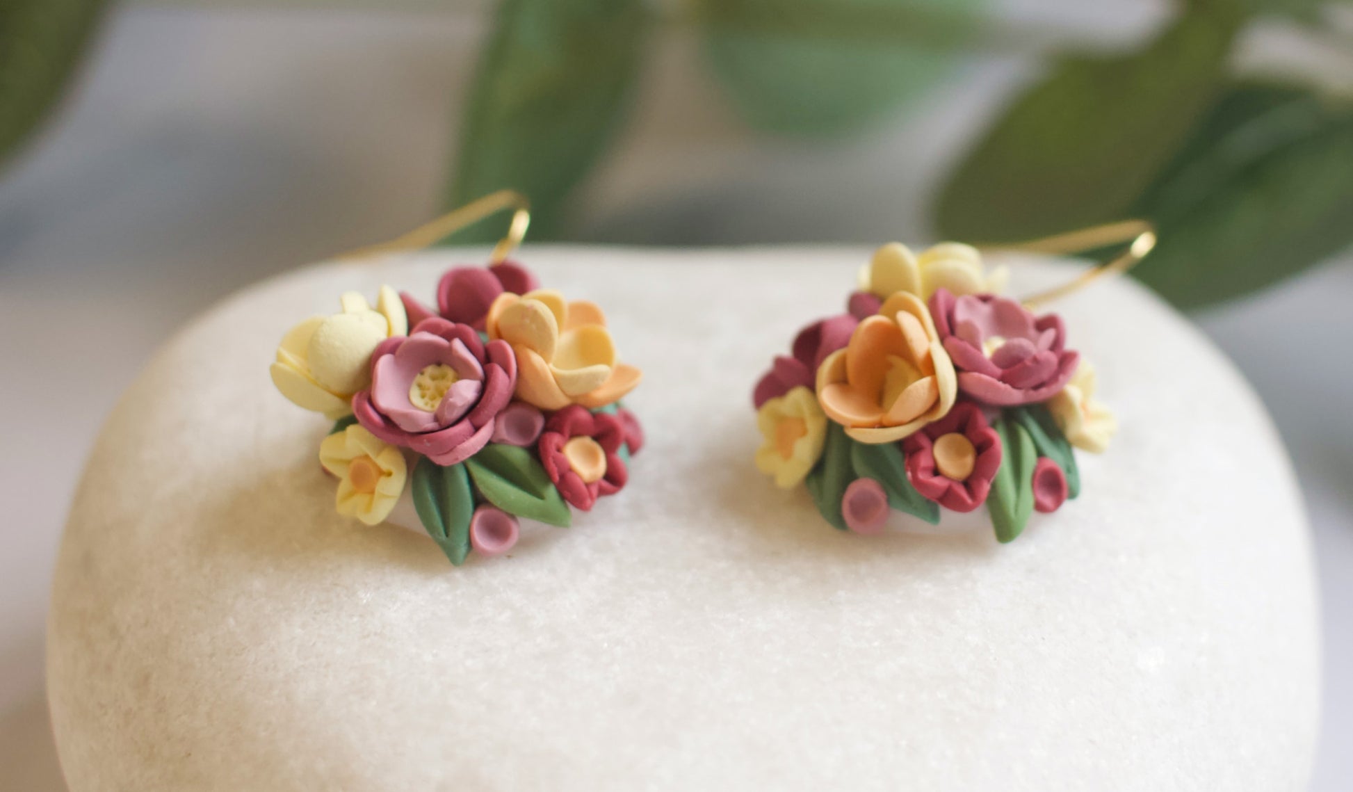 Floral earrings on a white stone surface with greenery in the background