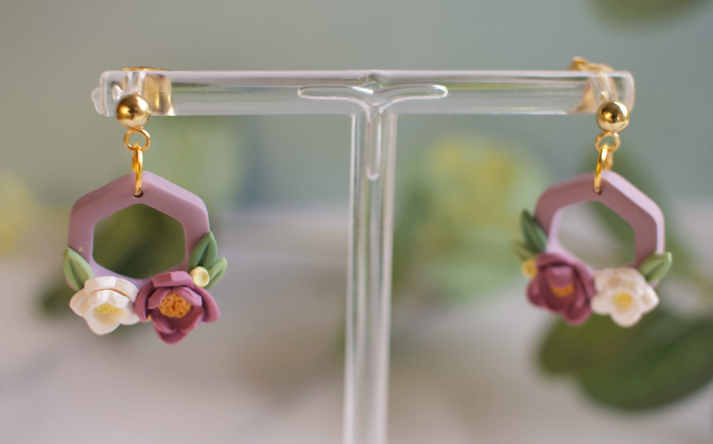Pair of floral hexagon earrings on a clear stand with a blurred background