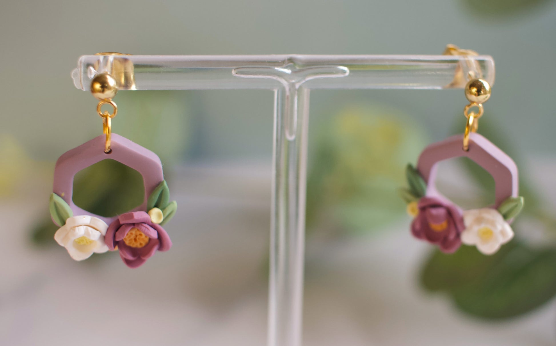 Pair of floral hexagon earrings on a clear stand with a blurred background