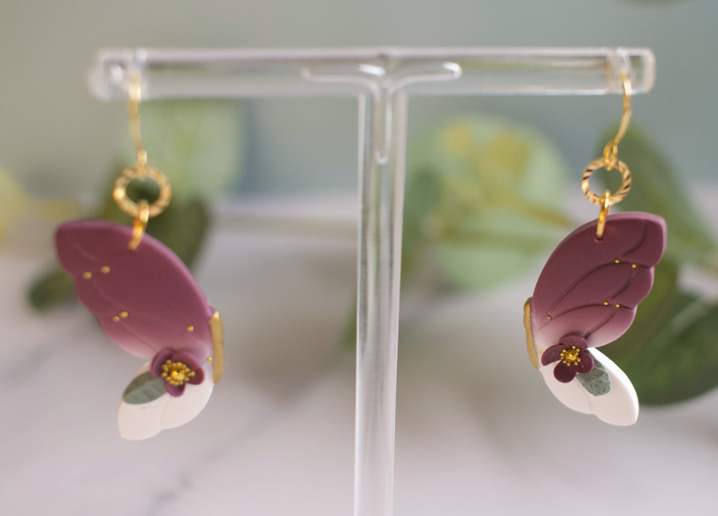 Pair of butterfly earrings with purple and white floral designs on a clear stand.