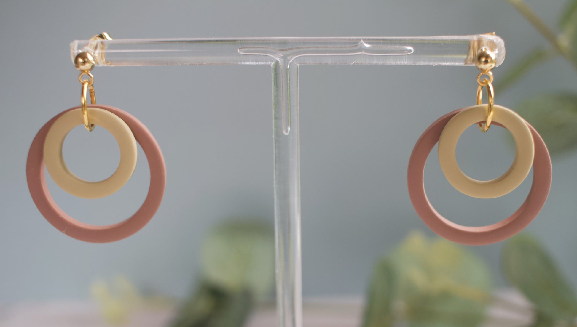 Pair of earrings with brown and beige circular designs on a clear stand against a blurred green background.