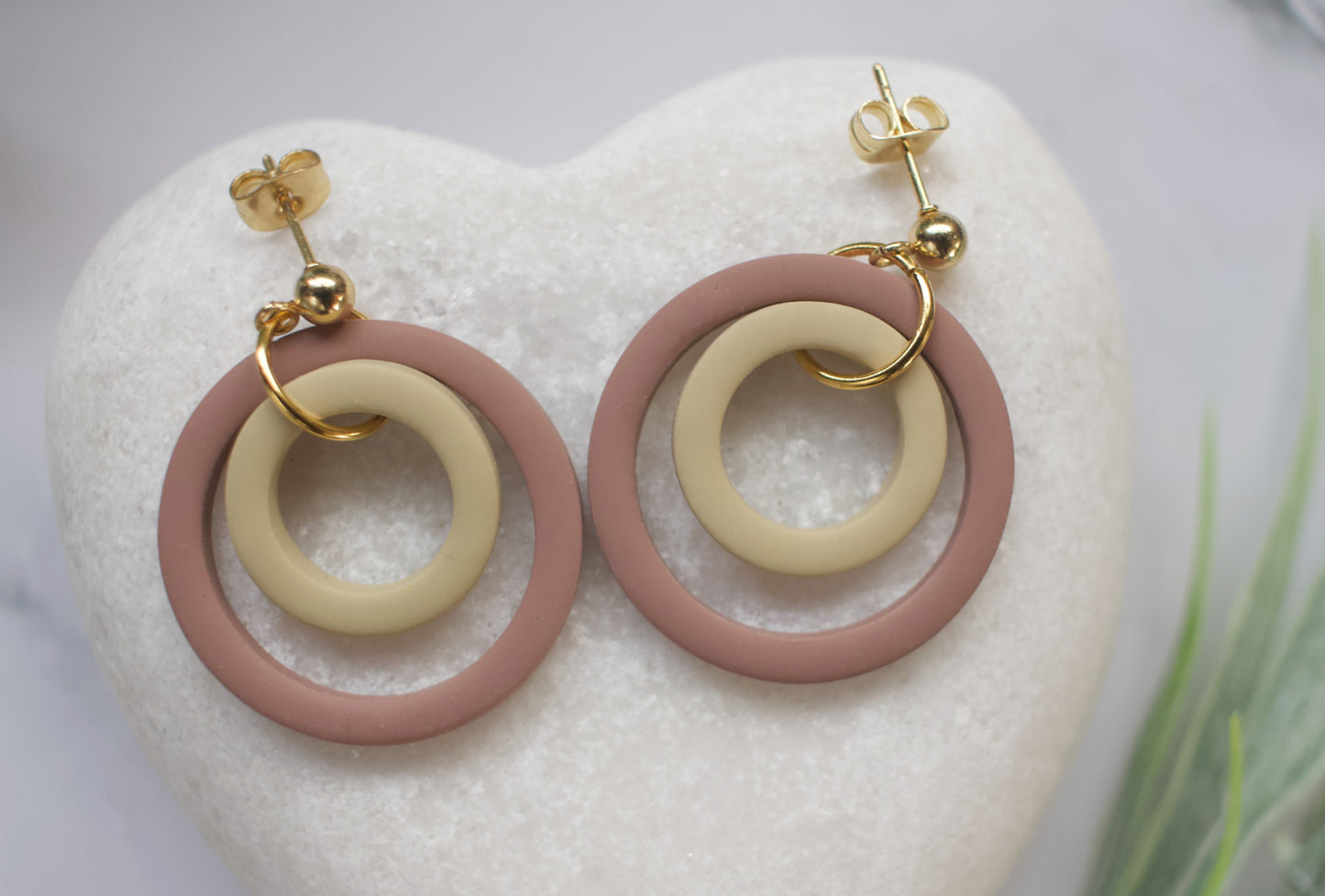 Pair of earrings with brown and beige circular designs on a white heart-shaped stone.