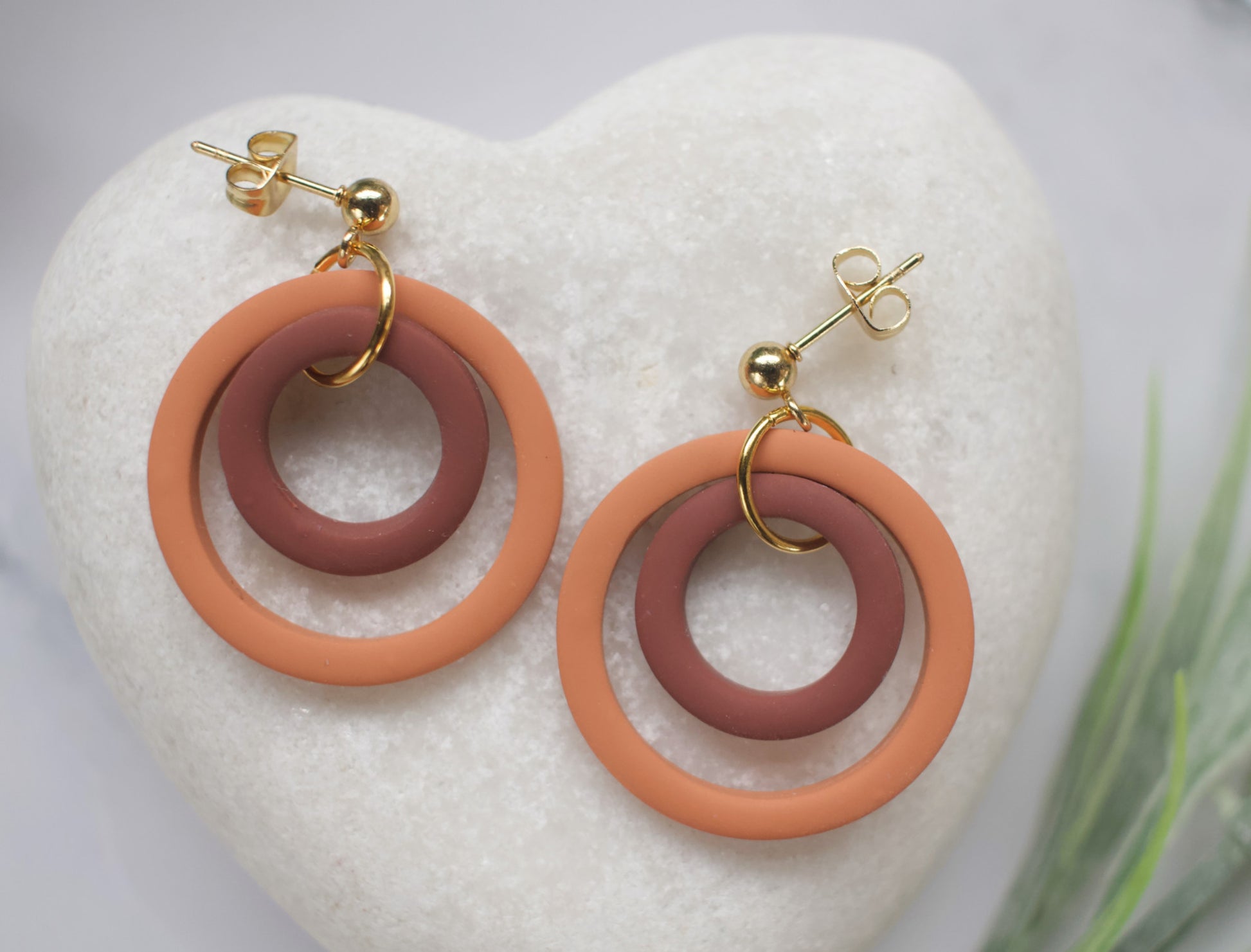 Pair of earrings with two circular rings in orange and brown on a white heart-shaped stone.