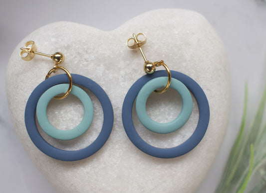 Pair of earrings with blue and turquoise circular design on a white stone background
