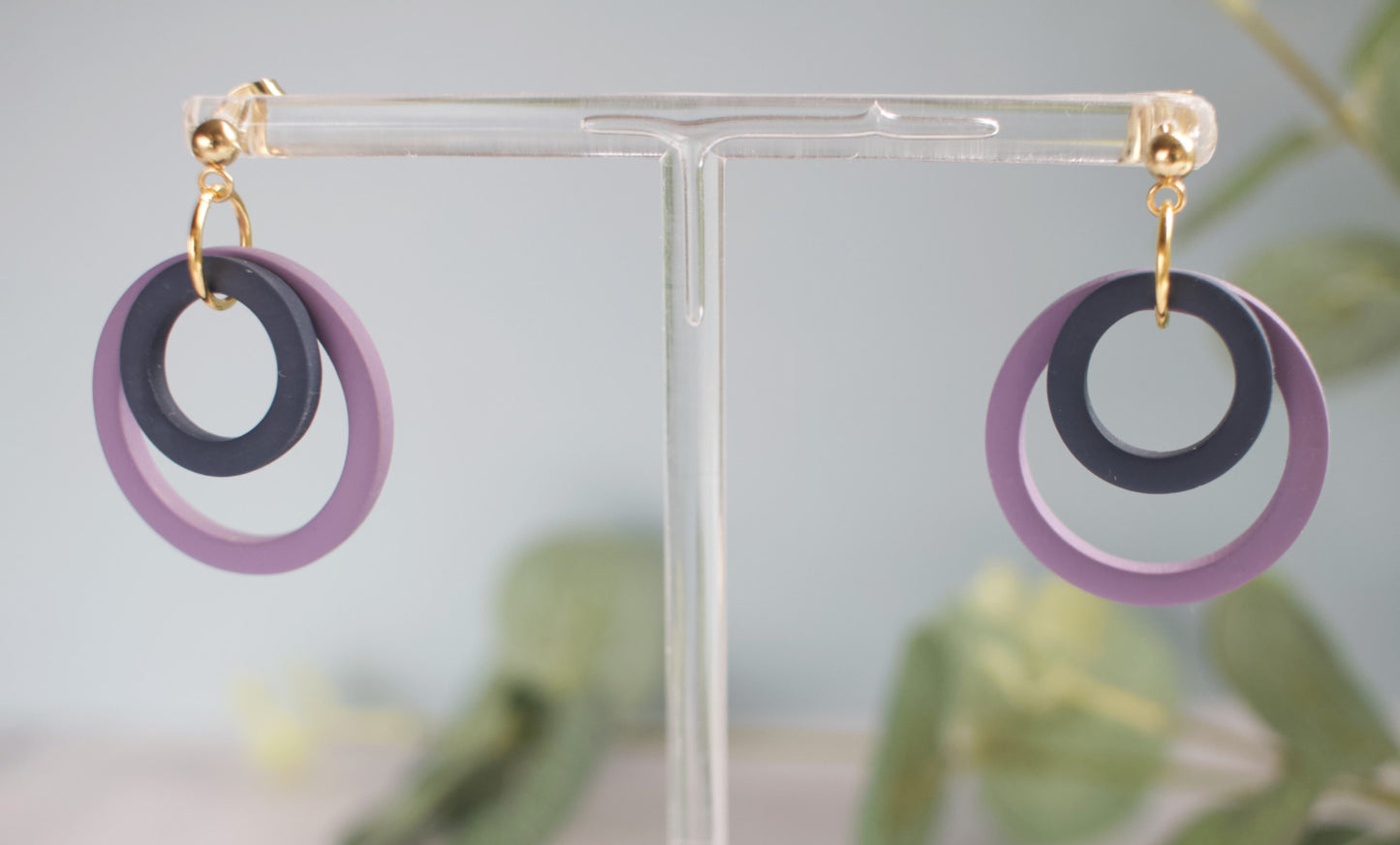 Earrings with purple and navy circular design on a clear stand against a neutral background