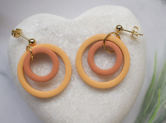 Pair of earrings with yellow and orange rings on a white stone background