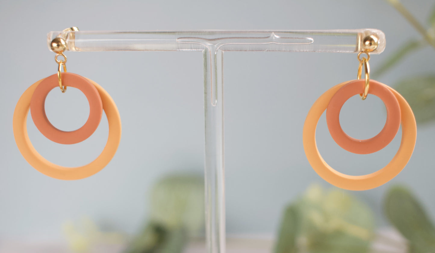 Pair of earrings with orange and yellow loops on a clear stand against a blurred green background