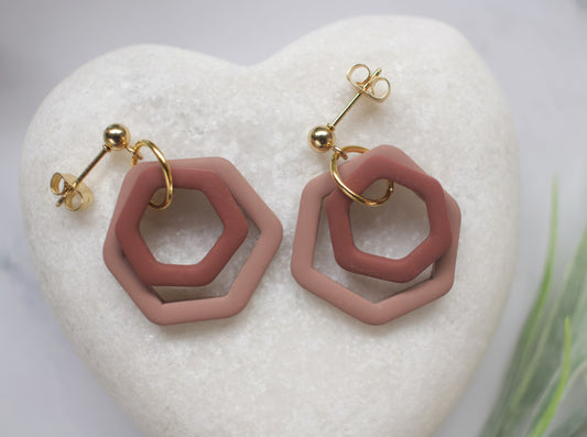 Brown hexagonal earrings with gold accents on a white heart-shaped stone.
