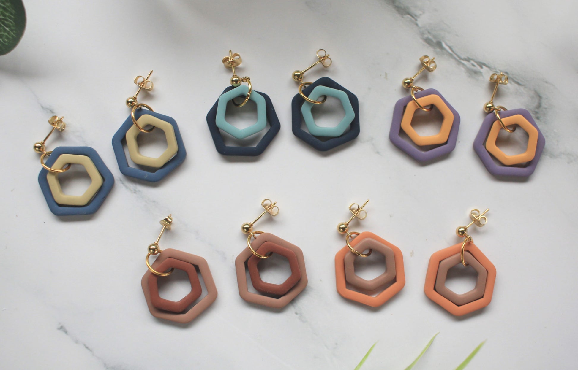 Hexagonal earrings in various colors on a marble surface