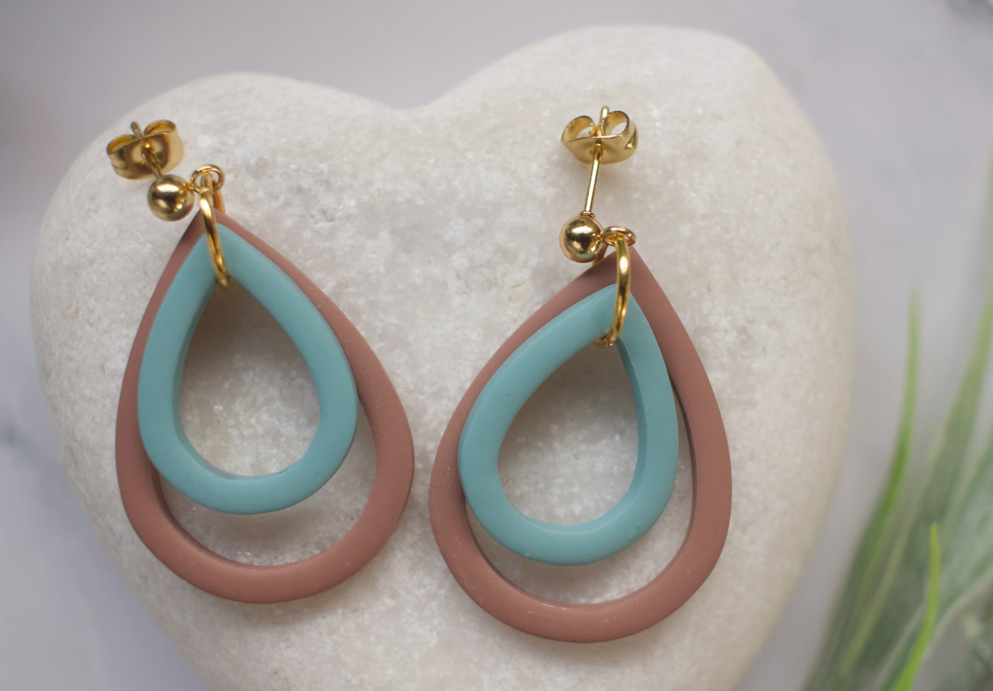 Teal and brown earrings with gold posts on a white heart-shaped stand.