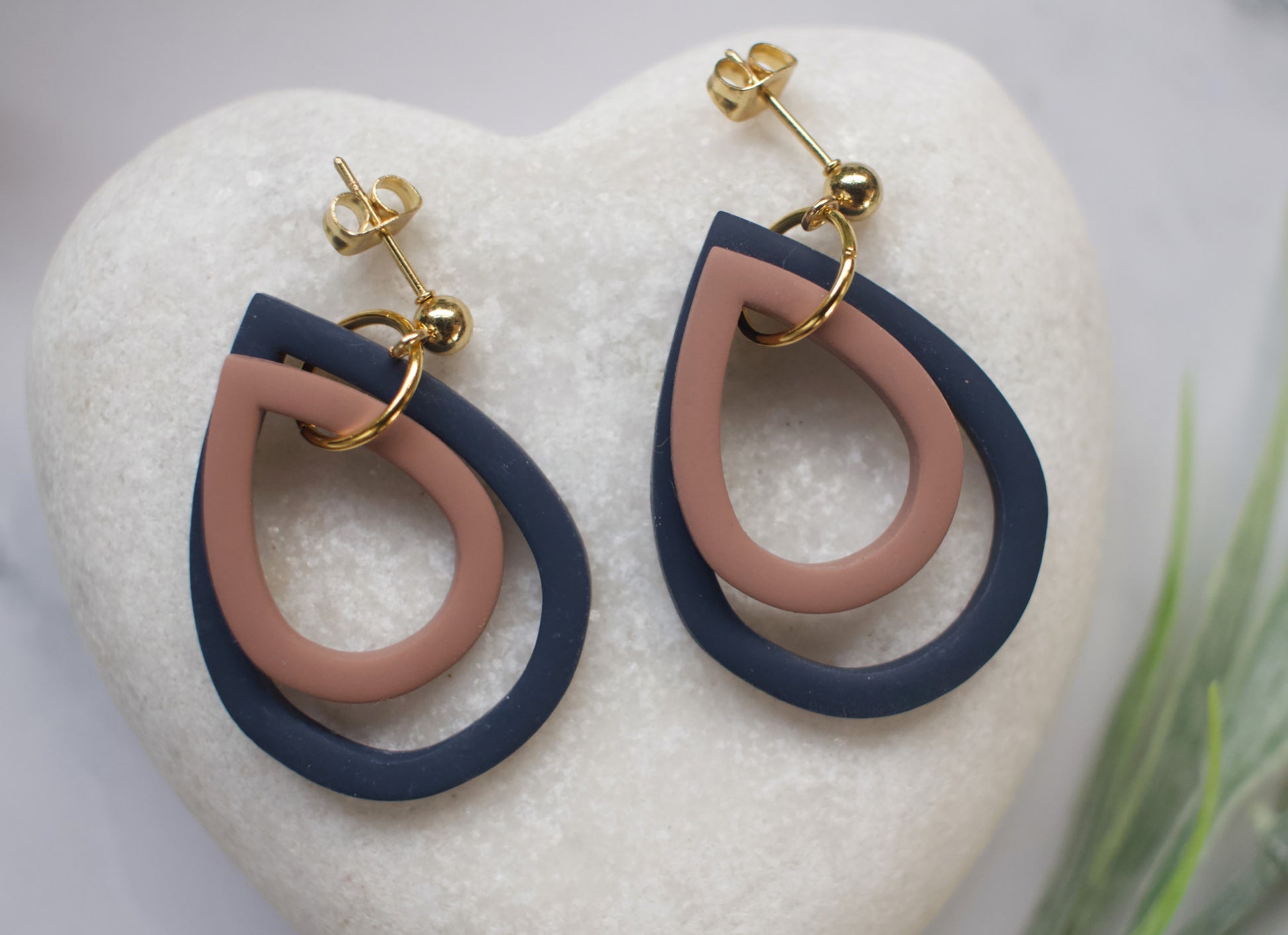 Pair of earrings with brown and blue tear drop design on a white heart-shaped stand.