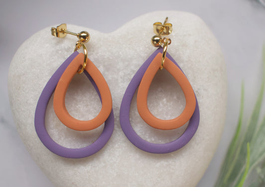 Pair of earrings with purple and orange teardrop design on a white heart-shaped object.