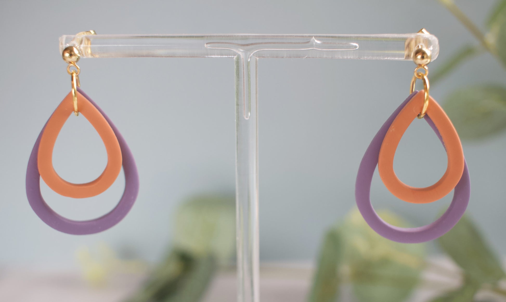 Pair of earrings with orange and purple loops on a clear stand against a light background