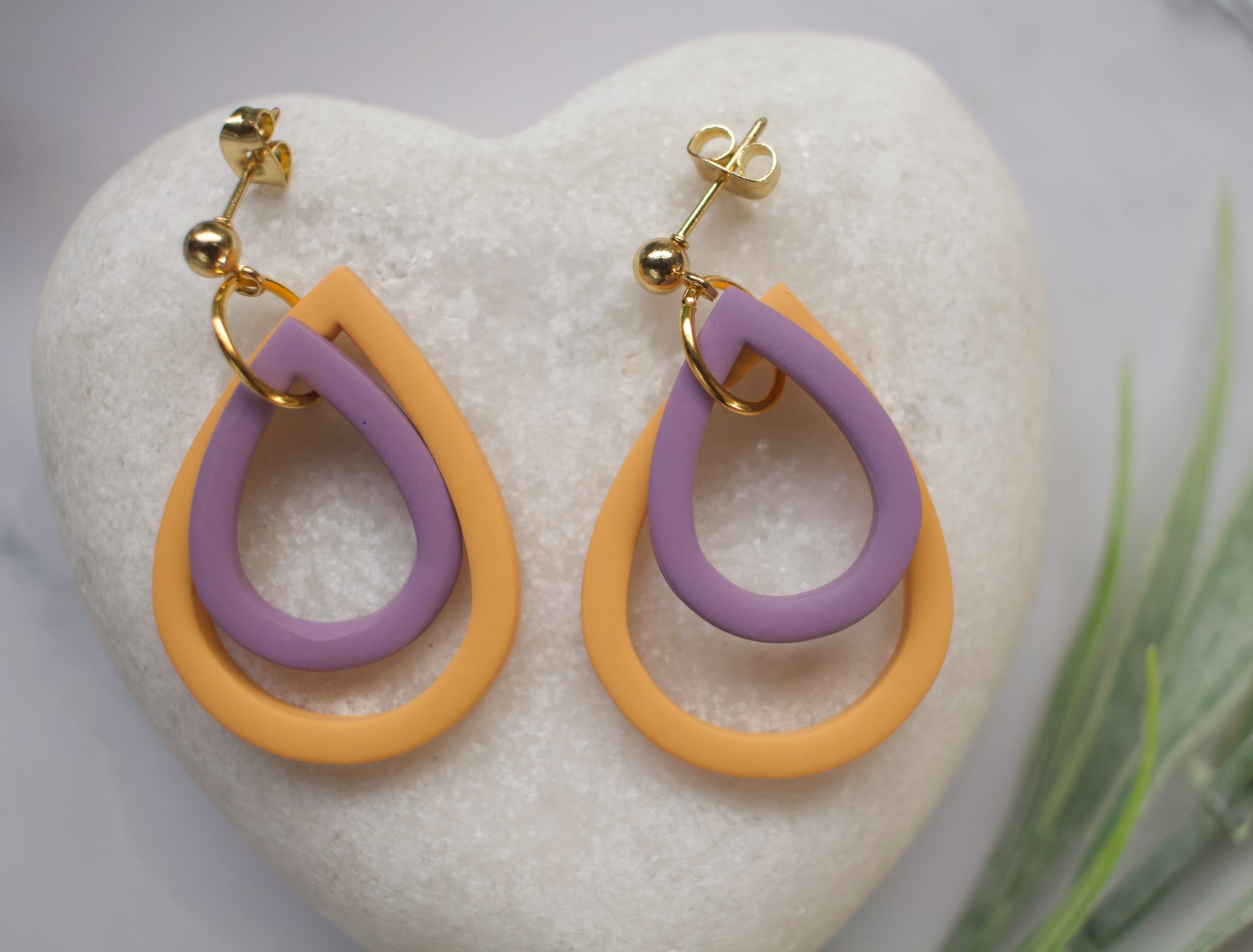 Pair of tear drop shaped earrings with purple and yellow loops on a heart-shaped stone.