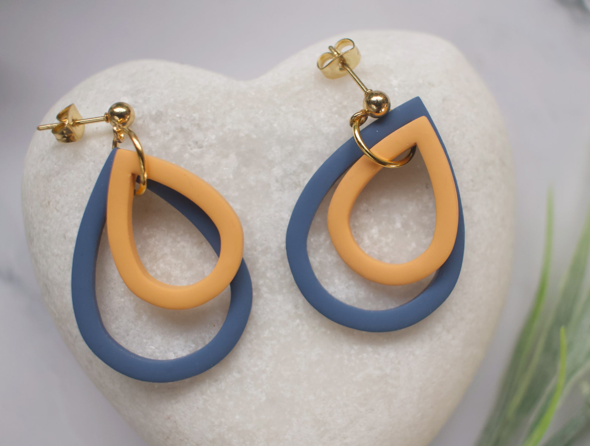 Pair of earrings with blue and yellow loops on a white stone surface