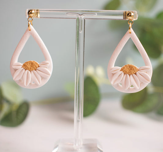 Pink teardrop earrings with gold accents on a clear stand against a blurred green leaf background