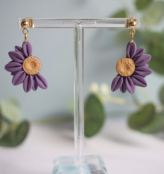 Purple flower-shaped earrings on a clear stand with a blurred greenery background