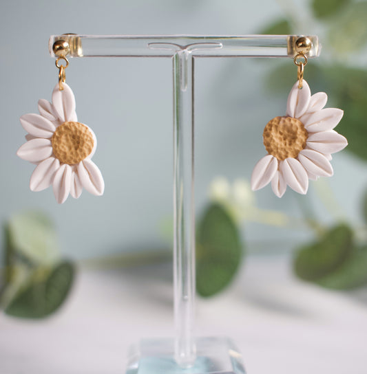 Flower-shaped earrings on a clear stand with a blurred greenery background
