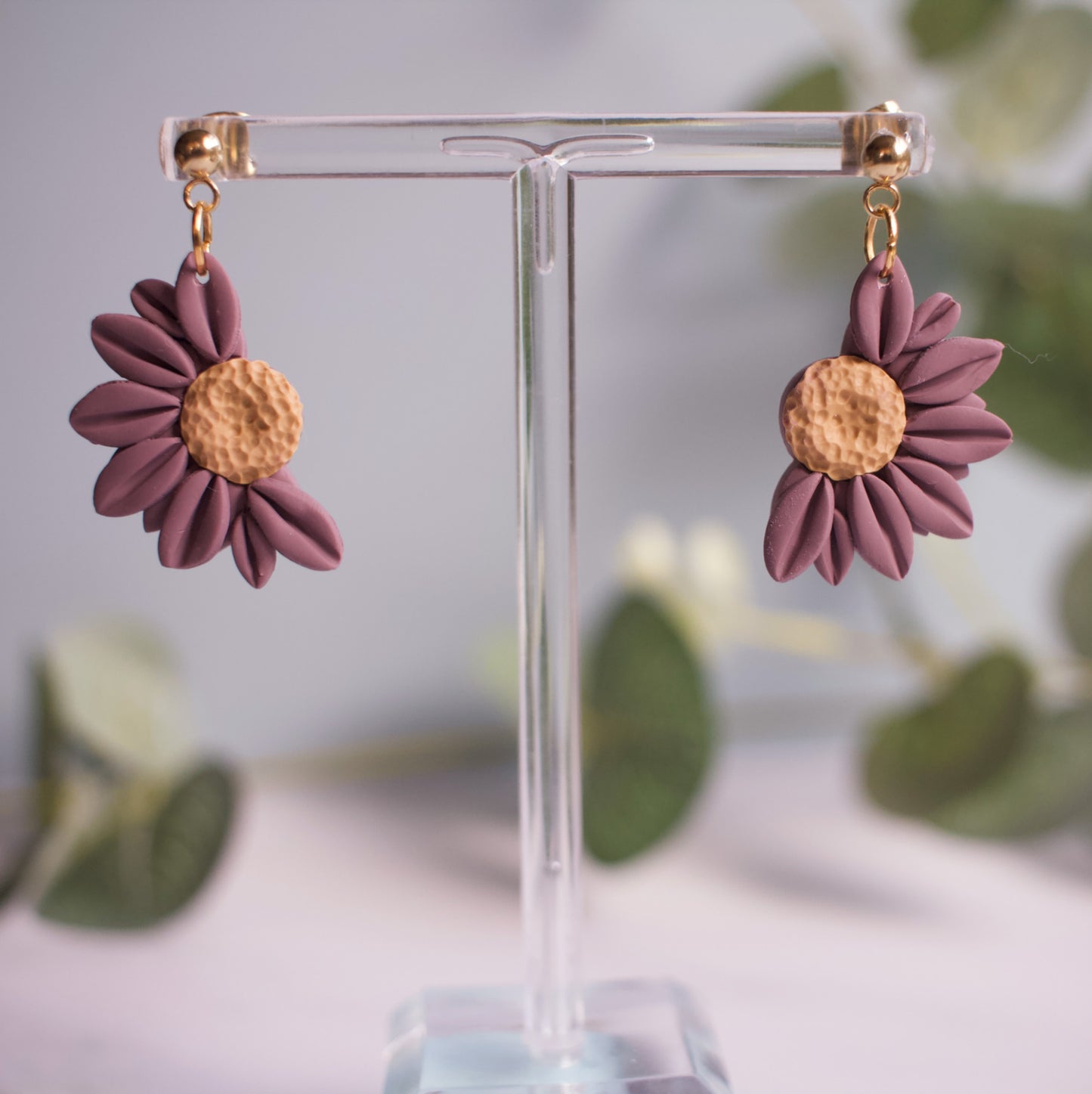 Flower-shaped earrings on a clear stand with a blurred green leafy background