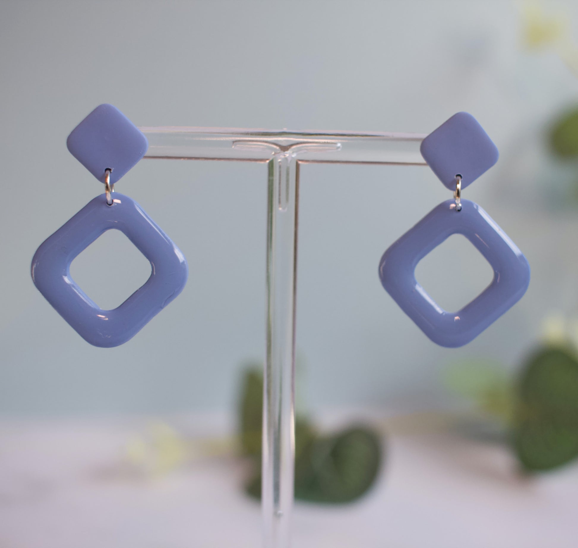 Pair of blue square-shaped earrings on a clear stand with a blurred background