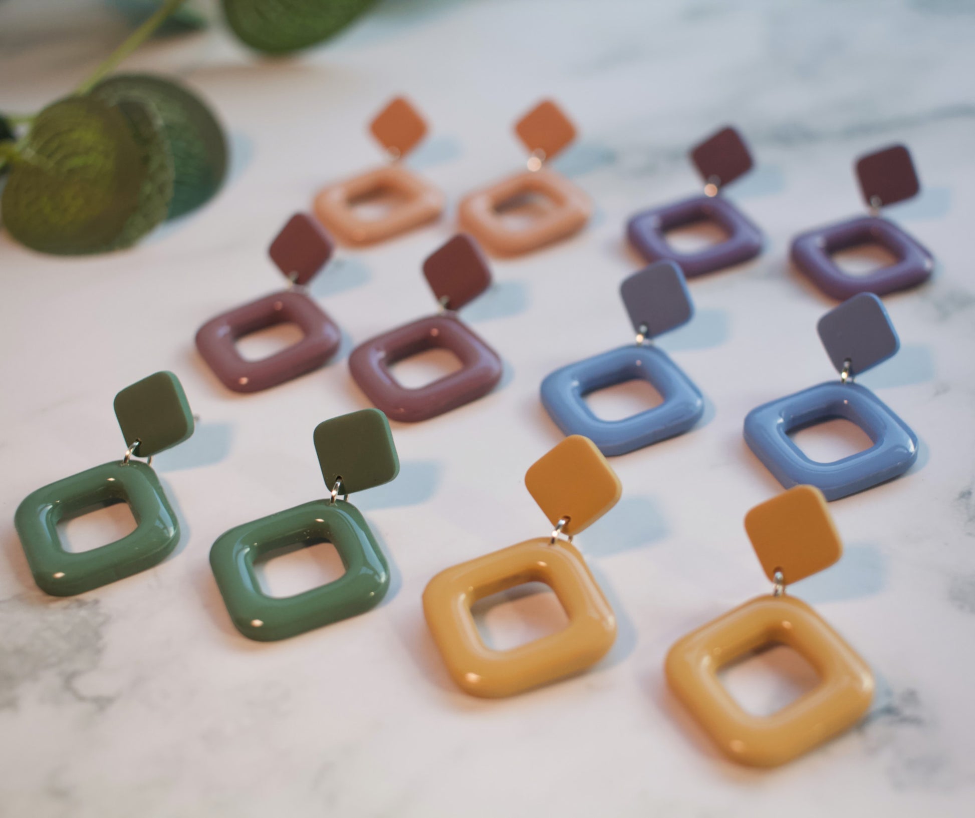 A collection of colorful square-shaped earrings on a marble surface