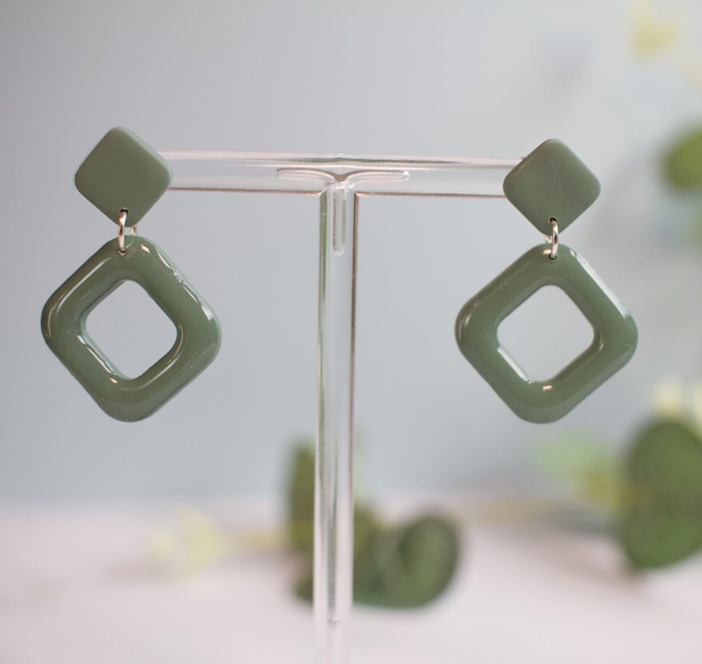 Green square-shaped earrings on a clear stand with a blurred background