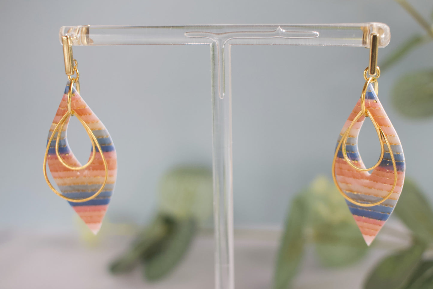 Colorful teardrop earrings on a clear stand with a blurred green plant background