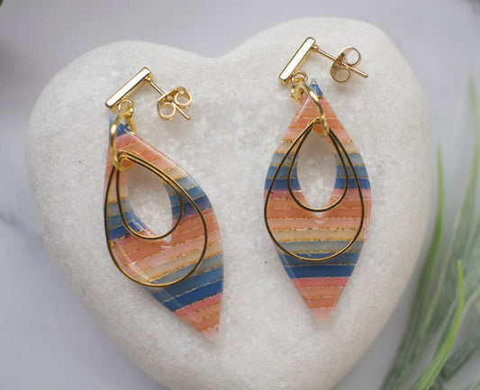 Colorful teardrop earrings with gold accents on a white heart-shaped stone.