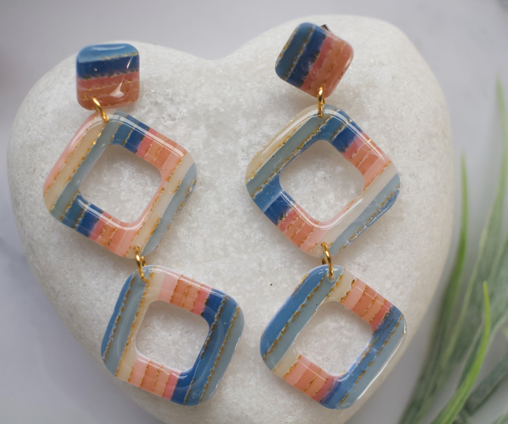 Colorful square-shaped earrings on a white stone with grass in the background