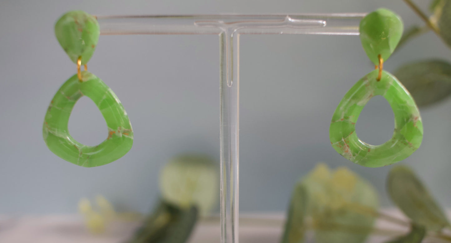 Green earrings on a clear stand with a blurred background