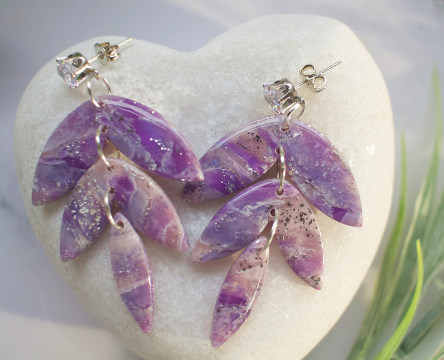 Purple leaf-shaped dangle earrings on a heart-shaped stone with grass in the background