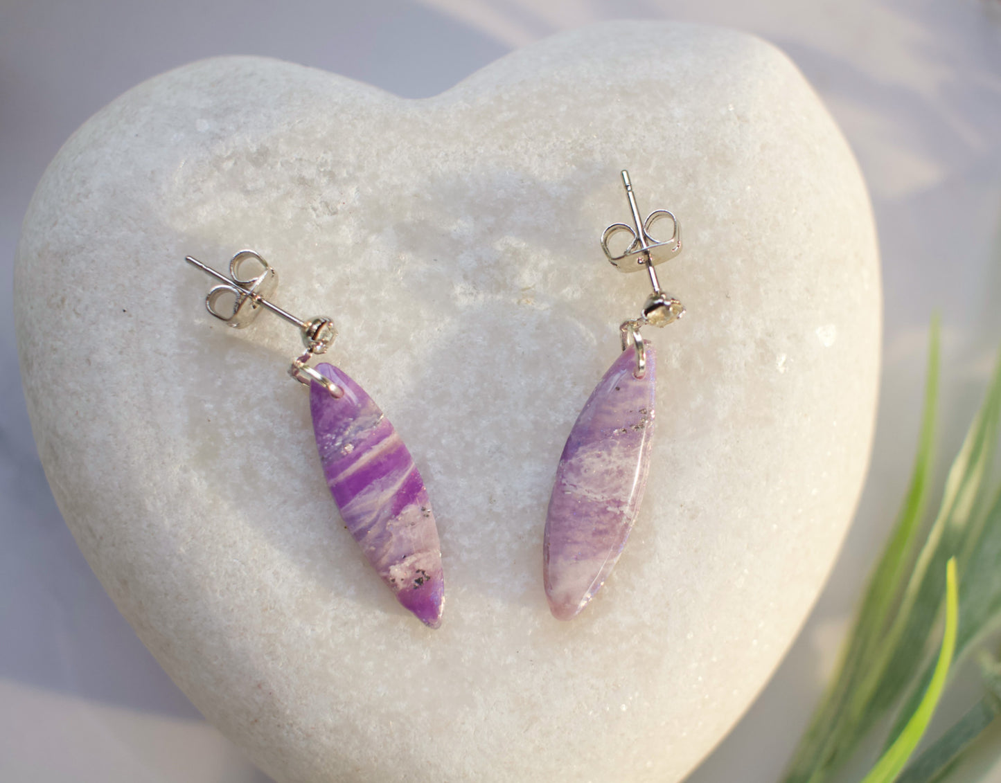 Purple teardrop earrings on a heart-shaped stone with grass in the background