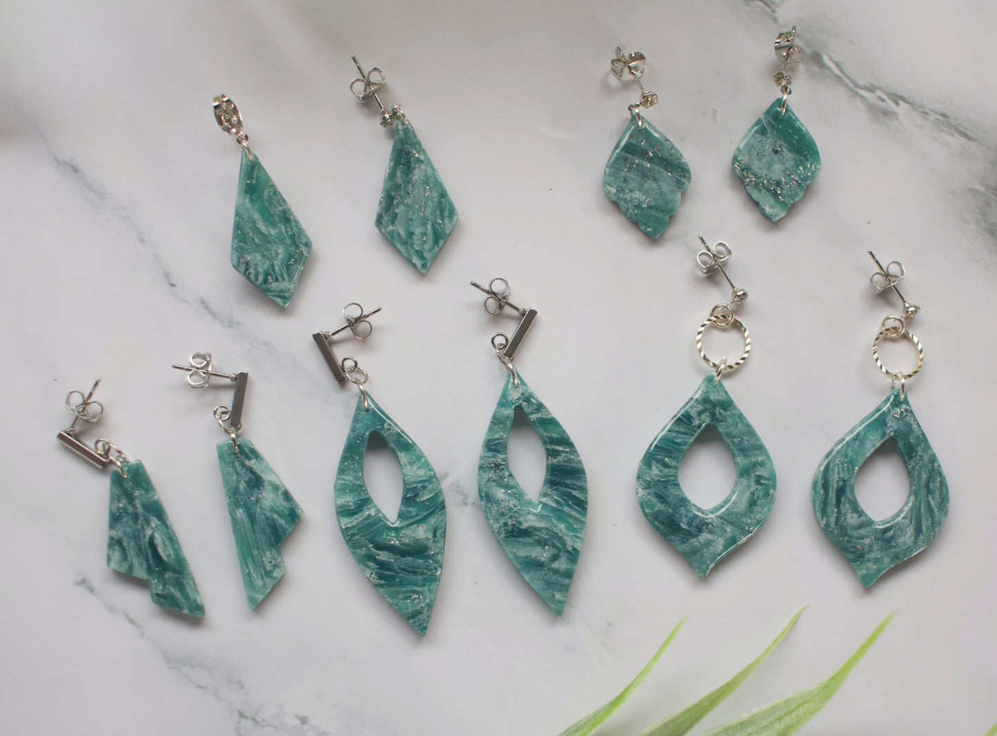 Teal marbled earrings on a marble surface