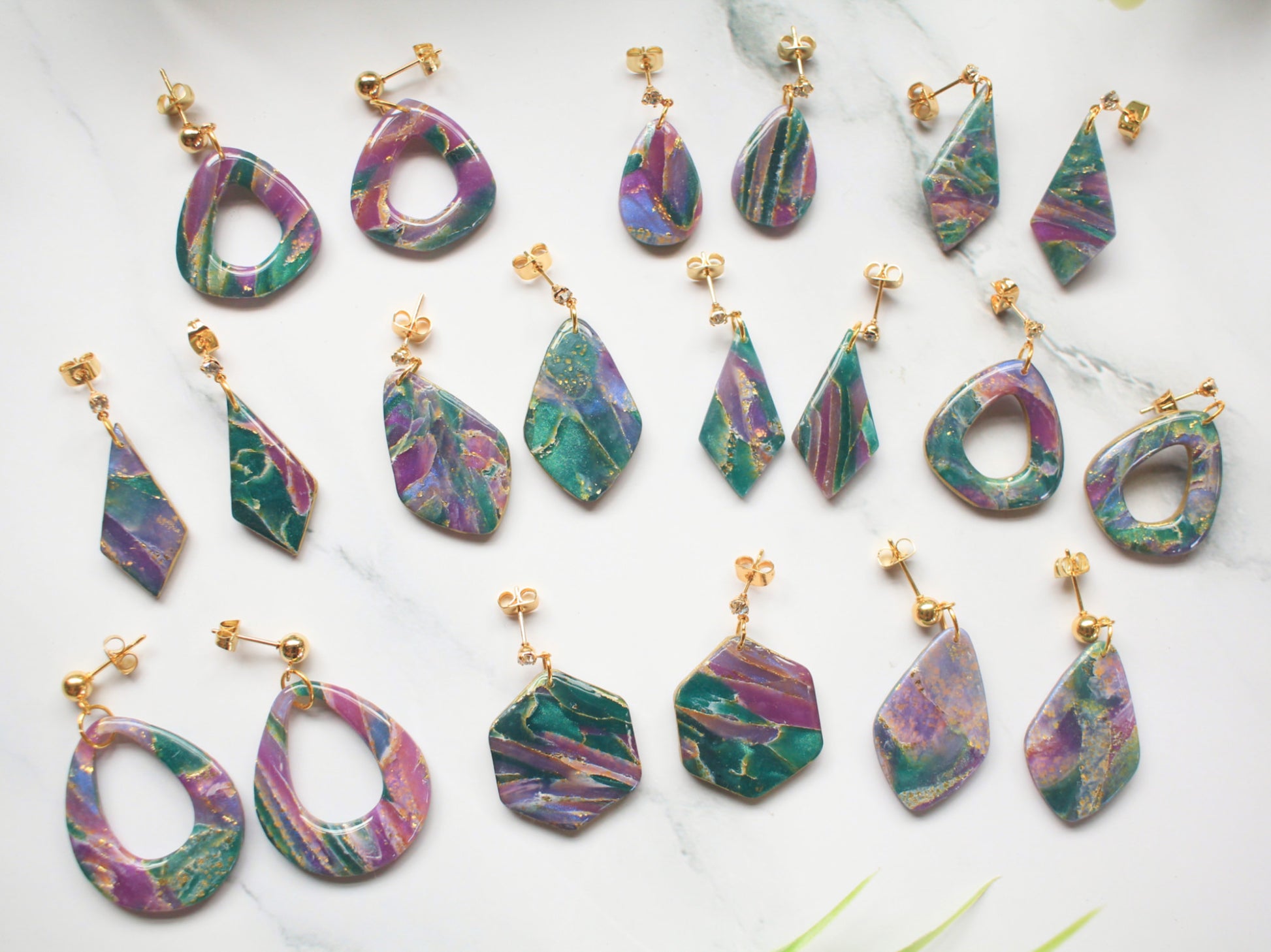 Purple, teal and gold marbled earring collection on a white background