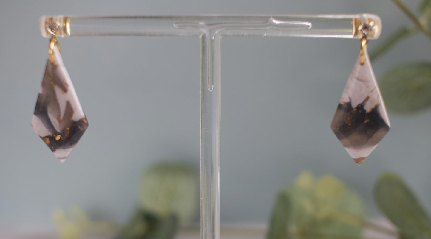 Teardrop-shaped earrings on a clear stand with a blurred green plant background