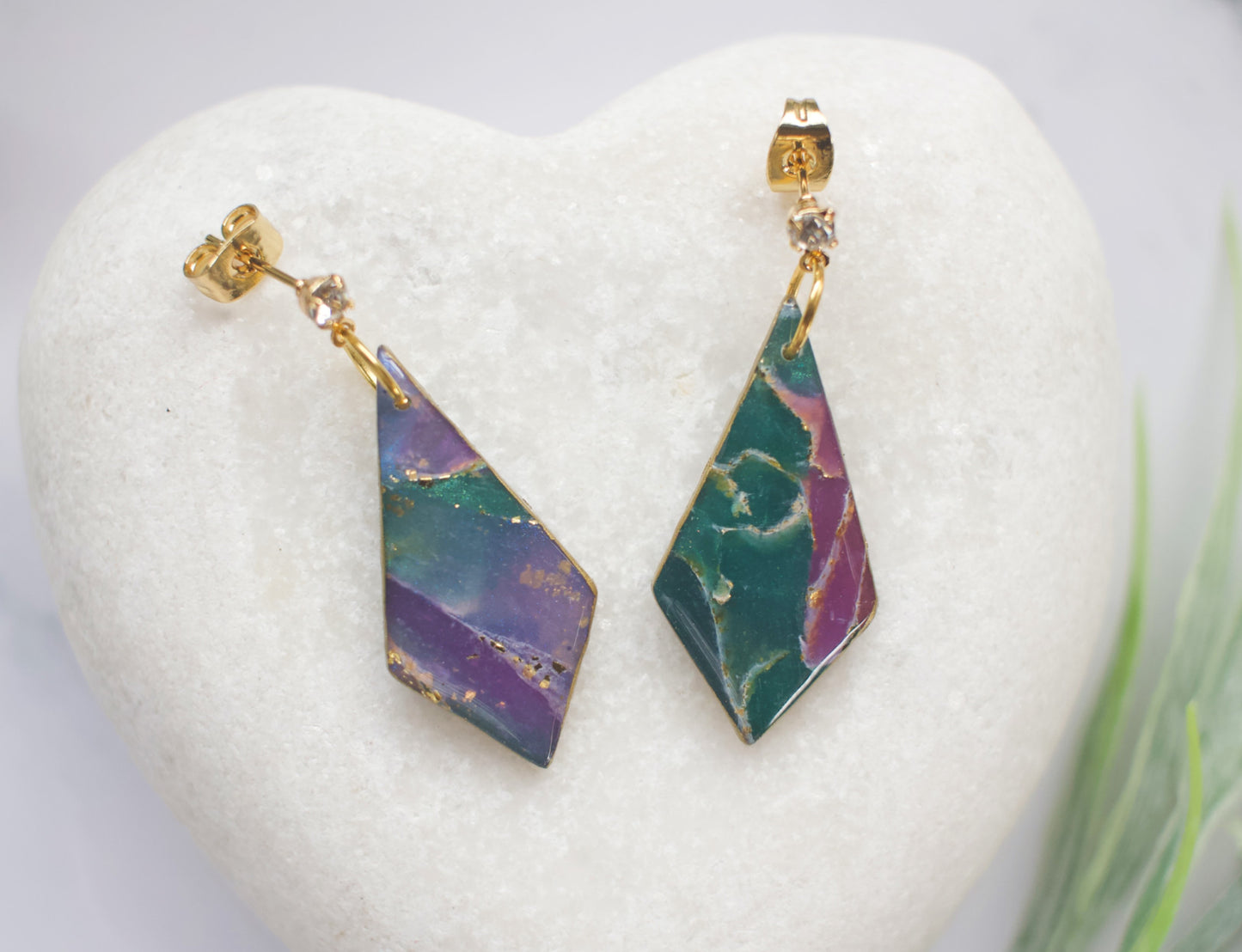 Geometric earrings with purple and green design on a white heart-shaped stand.