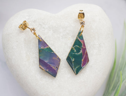 Geometric earrings with purple and green design on a white heart-shaped stand.